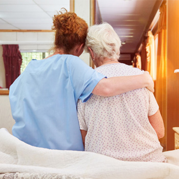 Younger women with red hair with her arm around older woman on hospital bed.